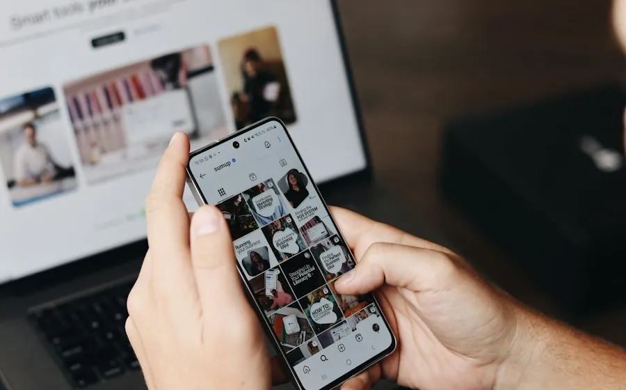 A hand holding a phone showing an Instagram feed in front of a laptop